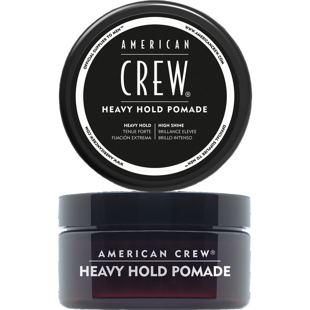 Translucent dark amber jar labeled American Crew Heavy Hold Pomade with its black lid removed and displayed above it, on a light grey backdrop.