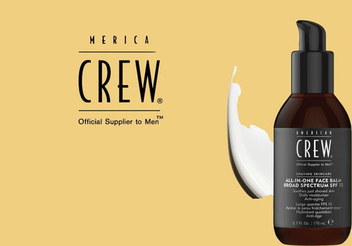 Amber pump bottle labeled American Crew All-In-One Face Balm Broad Spectrum SPF 15, with black pump cap, beside a smear of white cream on a mustard-yellow backdrop with the American Crew logo.