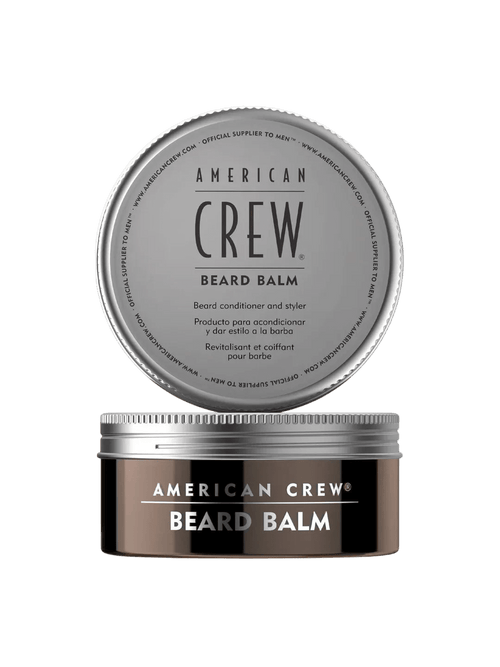 Round bronze-brown tin labeled American Crew Beard Balm with its silver screw lid removed and displayed above it, on a light grey backdrop.