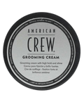 Top-down view of a round black tin lid with a silver American Crew Grooming Cream label, on a light grey backdrop.