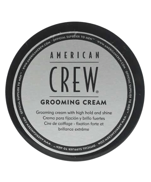 Top-down view of a round black tin lid with a silver American Crew Grooming Cream label, on a light grey backdrop.