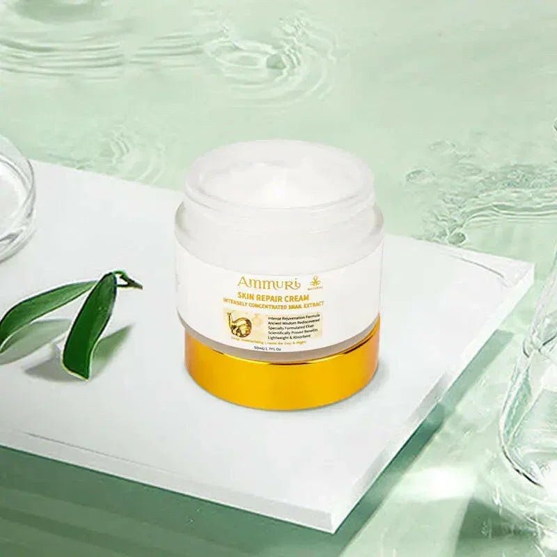 Open jar of white cream with a gold base band, labeled Ammuri Skin Repair Cream, Intensely Concentrated Snail Extract, with printed text reading Intense Rejuvenation Formula, Ancient Wisdom Rediscovered, Specially Formulated Elixir, and Scientifically Proven Benefits, 50ml/1.7Fl.Oz, staged on a white block with a green leaf and water backdrop.