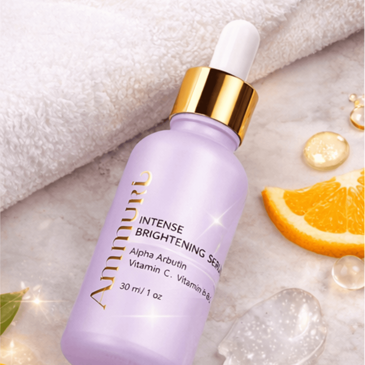 Light purple dropper bottle with gold collar and white dropper cap labeled Ammuri Intense Brightening Serum, Alpha Arbutin, Vitamin C, Vitamin B, 30 ml/1 oz, lying on a marble surface beside a white towel, an orange slice, and clear gel droplets.