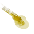 Close-up of a glass dropper releasing a pale golden serum that pools on a light grey background