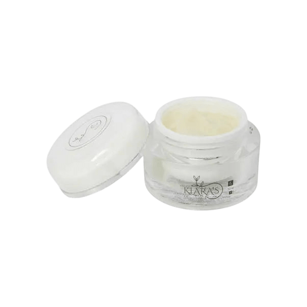 Open clear glass jar of pale-yellow cream with its white lid resting beside it, small label reading "Klara's" on the jar, against a plain light gray background.